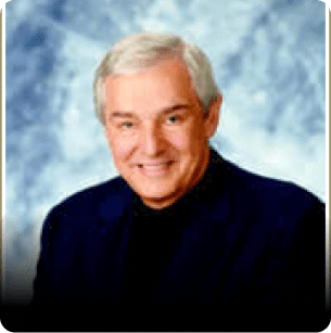 A man with white hair and wearing a black suit.